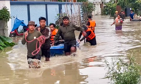 People walk through a flooded area after heavy rains, in Imphal East
