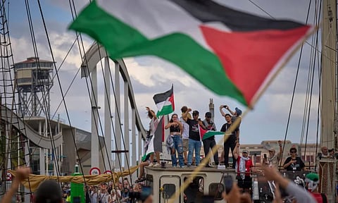 Activists wave on a boat taking part in a civilian flotilla bound for Gaza, aiming to break the Israeli blockade and deliver humanitarian aid, in Barcelona, Spain (AP Photo)