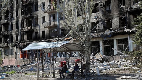 Local residents sit on a bench near an apartment building damaged during Ukraine-Russia conflict in the southern port city of Mariupol, Ukraine