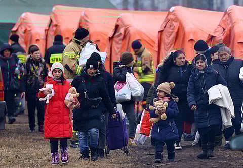 People walk past tents on their way to board a train after crossing the border from Ukraine to Poland