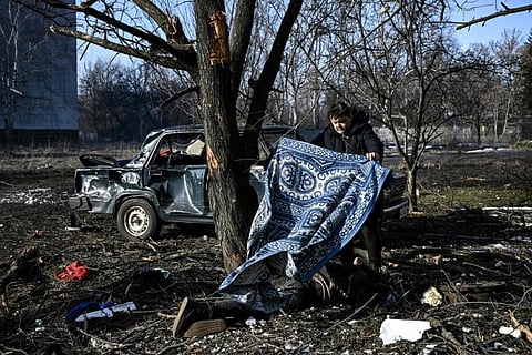 A man uses a carpet to cover a body on the ground after bombings in Chuguiv