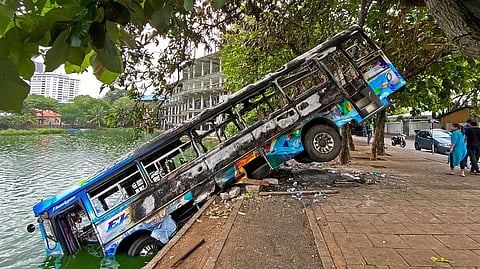 People walk past a burnt bus near Sri Lankas former prime minister Mahinda Rajapaksa's official residence
