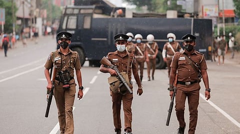 Sri Lankan police officers with tear gas guns walk along a main road as people protest
