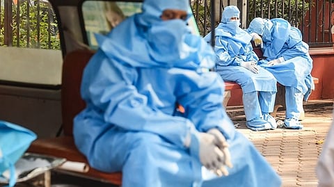 Family members, wearing PPE kits, wait during cremation of a COVID-19 victim, at the Nigambodh Ghat in New Delhi