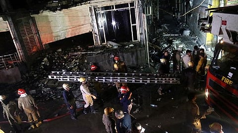 Fire fighters carry a ladder at the site a fire that broke out at a commercial building in Delhi's western suburb