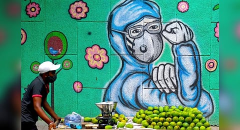 A fruit vendor pulls his cart as he walks past a wall mural depicting a front-line Covid-19 worker