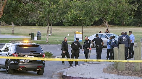 Police officers stand near the scene of a shooting as pedestrians pass by at Peck Park in San Pedro, Calif.