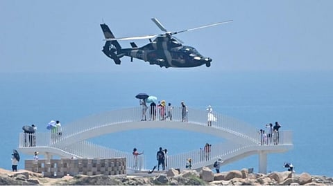 Tourists look on as a Chinese military helicopter flies past Pingtan island, one of mainland China's closest point from Taiwan, in Fujian province on August 4, 2022, ahead of massive military drills off Taiwan following US House Speaker Nancy Pelosi'