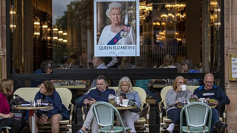 People sit at a terrace bar next to a portrait of Queen Elizabeth II