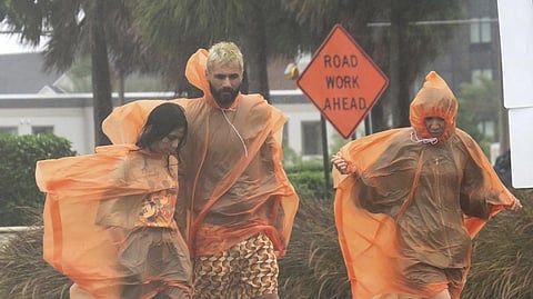 People in raincoats walk along International Drive in Orlando, Fla., Wednesday, Sept. 28, 2022, as the first effects of Hurricane Ian are felt in central Florida.