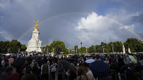 People gather outside Buckingham Palace in London as a double rainbow appears in the sky.