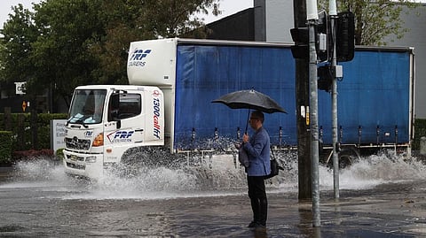 A pedestrian stands on the corner of a flooded street as heavy rains affect Sydney
