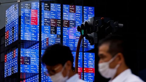 People pass by an electronic screen showing Japan's Nikkei share price index inside a conference hall in Tokyo