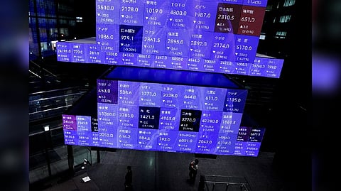 Visitors walk past Japan's Nikkei stock prices quotation board inside a conference hall in Tokyo