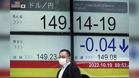 A person wearing a protective mask walks past an electronic stock board showing Japan's Yen/U.S. Dollar exchange rate