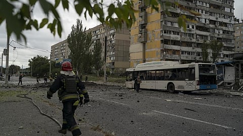 Firefighters and police officers work on a site where an explosion created a crater on the street