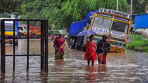Commuters wade through a waterlogged road amid rainfall