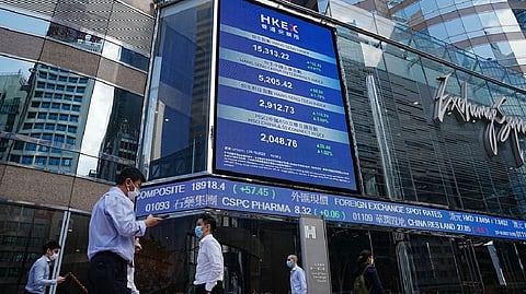 People walk past a screen displaying the Hang Seng stock index at Central district