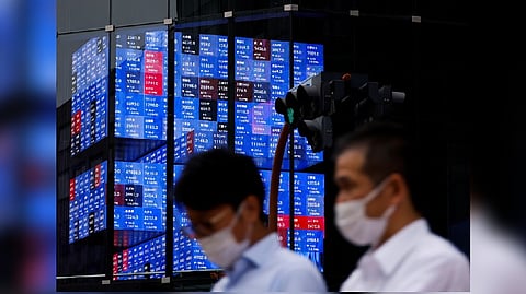 People pass by an electronic screen showing Japan's Nikkei share price index inside a conference hall in Tokyo