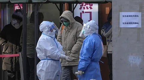 Medical workers in protective gear chat each other as residents wait to enter the fever clinic of a hospital in Beijing