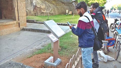 A visitor scanning a QR code in front of a monument in Mahabalipuram.