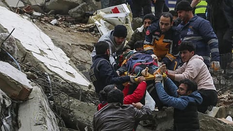 People and emergency teams rescue a person on a stretcher from a collapsed building in Adana, Turkey