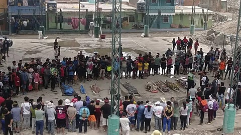 Residents stand around the bodies of persons who perished in recent landslides in Camana, Peru, Monday.