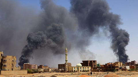 A man walks while smoke rises above buildings after aerial bombardment, during clashes between the paramilitary Rapid Support Forces and the army in Khartoum North
