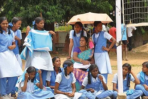 Students hold umbrella for a teacher at the Nethaji stadium in Vellore on Friday
