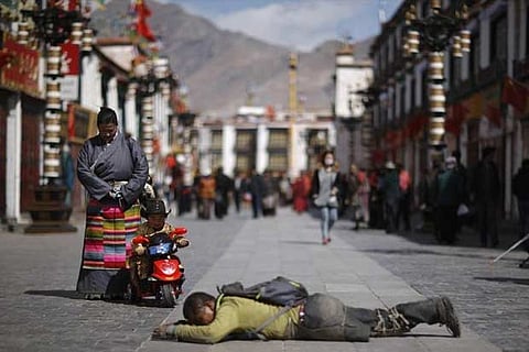 File photo of a child looking at a pilgrim kowtowing on a street outside Jokhang Monastery in Lhasa