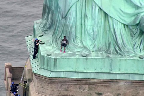 A police officer climbs up a ladder to talk to a  climber into descending the Statue of Liberty