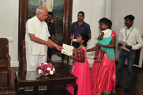 Governor Banwarilal Purohit hands over a greeting card to a visitor at Raj Bhavan