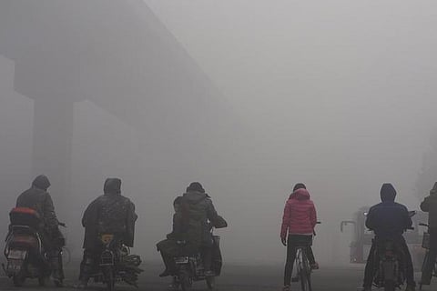 Residents on their bicycles and electric bikes wait for traffic at an intersection amid heavy smog
