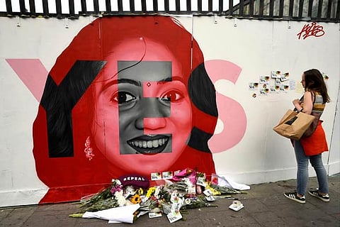 A woman looks at a new mural of Savita Halappanavar with flowers placed beneath it