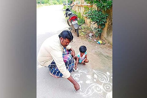 A man draws kolam on the road while his daughter lends a helping hand in the city on Monday
