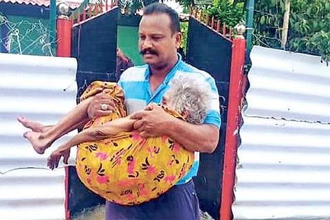 A rescue personnel carries an elderly woman out of a marooned house at Krishna Nagar in Thoothukudi