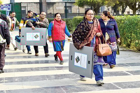 Polling officers carry EVM machines as they leave for their stations on the eve of the Delhi Assembly election