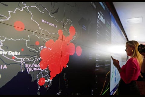 Source: Reuters/ A reporter stands in front of a coronavirus global map