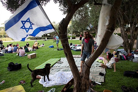 An Israeli flag flutters as people gather at a protest camp site (Reuters)