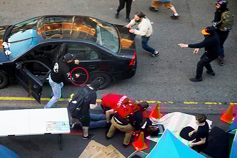 A man exits a vehicle with a gun as a man is tended to by medics after being shot