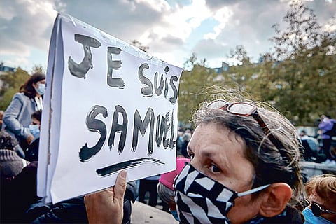 A protestor holds a sign memorializing a French teacher beheaded after showing students caricatures