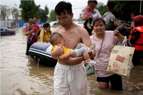 A man seen carrying a child through a flooded road in China (Credit: Reuters)