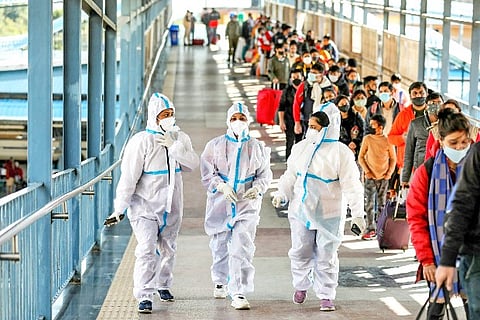 Health workers walk past passengers waiting in a queue during Covid-19 testing