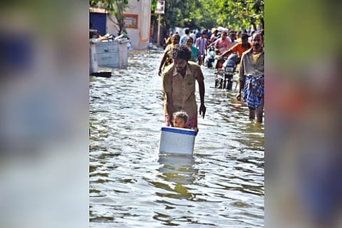 A man places his infant child in a box as he wades through an inundated street in Chennai on Friday