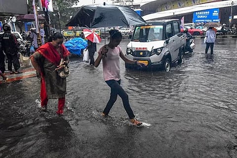 Pedestrians hold umbrellas while trying to cross a street in the heavy rain (Image credit: PTI)