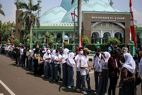 Students wearing protective masks stand in line to receive a vaccine dose