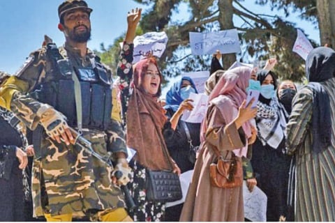 File Photo : A Taliban fighter passes by a group of women protesters in Kabul, on Tuesday