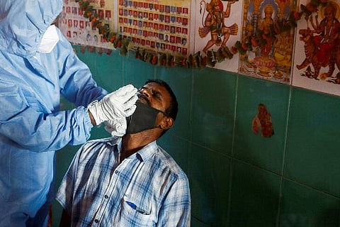 A health worker in personal protective equipment (PPE) collects a swab sample from a man