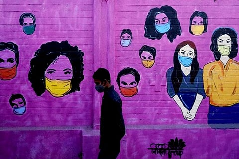 A man wearing a protective face mask walks past a mural on a street (Credit: Reuters)