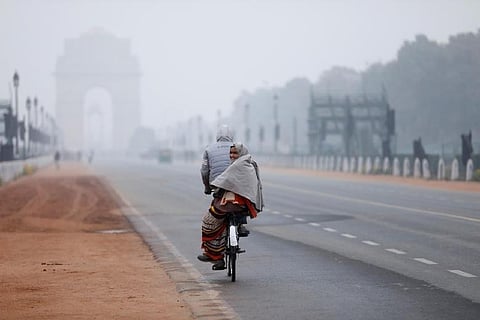 A woman sits behind a bicycle on a cold winter morning in New Delhi (Credit: Reuters)